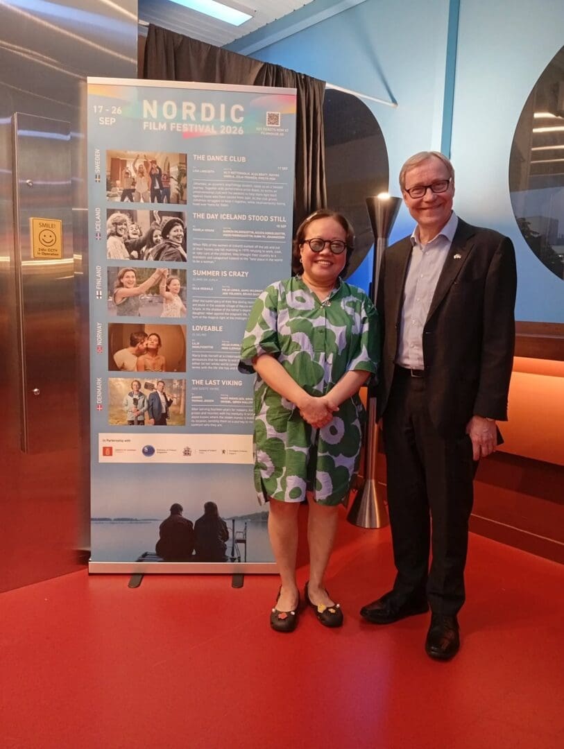 Current image: Two representatives standing beside a Nordic Film Festival 2026 programme display in Singapore.