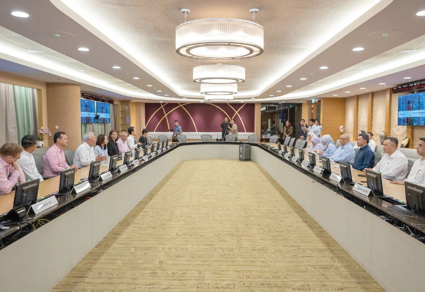 Brunei Crown Prince Al-Muhtadee Billah and members of the Temasek Holdings team sit around a conference table during a meeting. The room is equipped with presentation screens, individual monitors and meeting facilities.