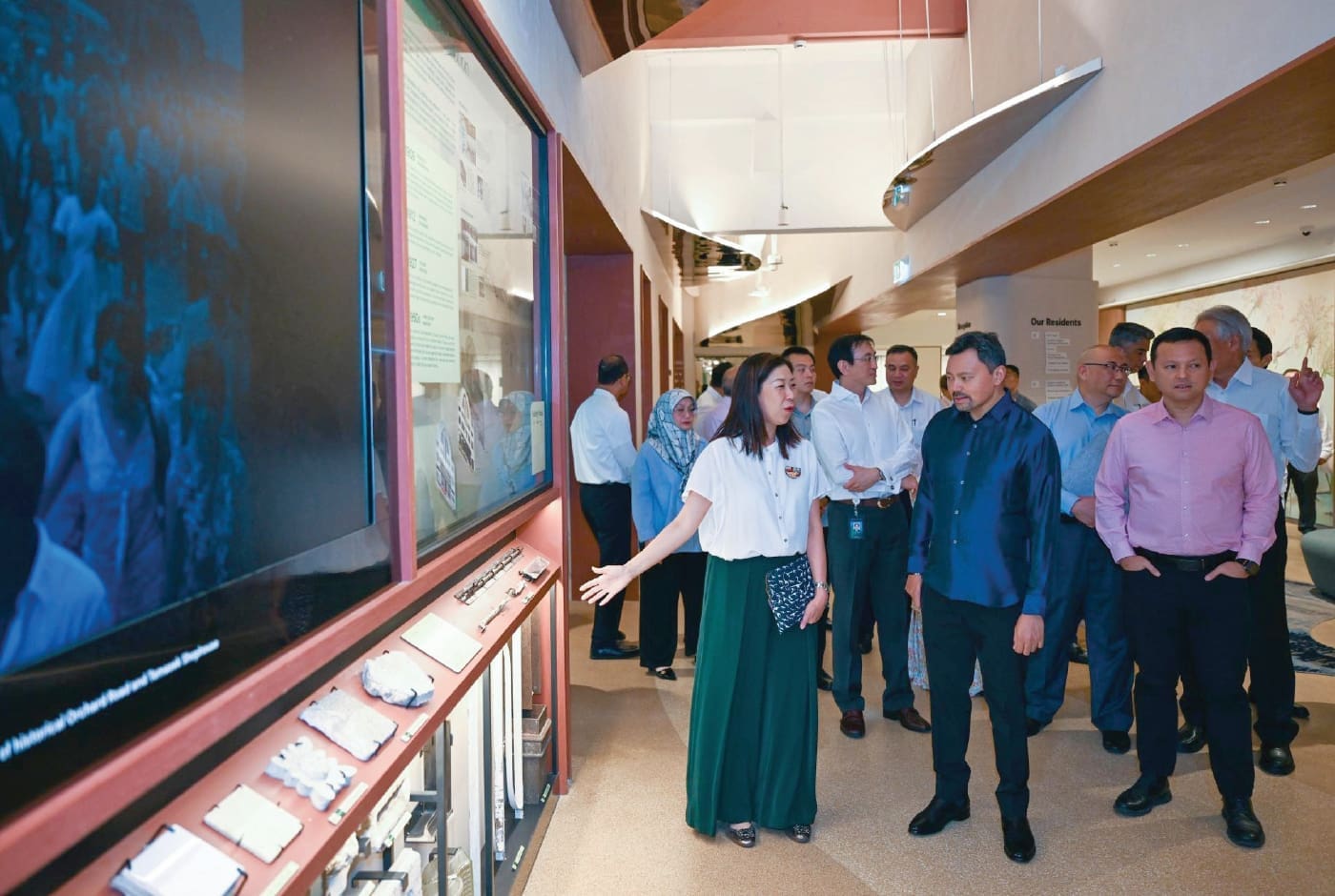 Brunei Crown Prince Al-Muhtadee Billah and accompanying officials walk through an exhibition area at Temasek Shophouse. A guide explains displays featuring historical and institutional information to the group.